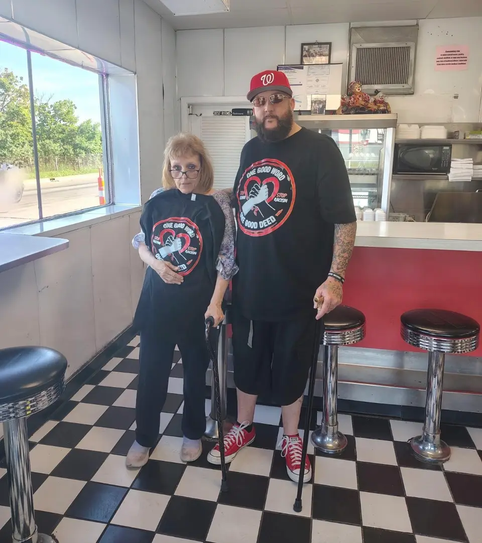 Two people wearing One Good Word One Good Deed shirts inside a diner.